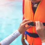Asian mother helping her son to wear life jacket before playing in swimming pool, Selective focus.