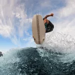beautiful view of a wakesurf board and a male athlete jumping in the air above a splashing wave